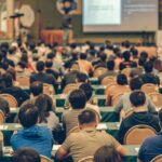 
                            a packed conference hall full of attendees watching a seminar                            